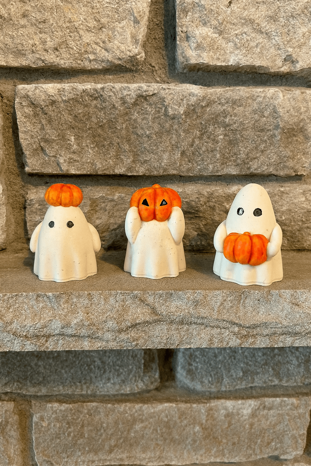 Three Halloween-themed figurines with pumpkins on a stone surface