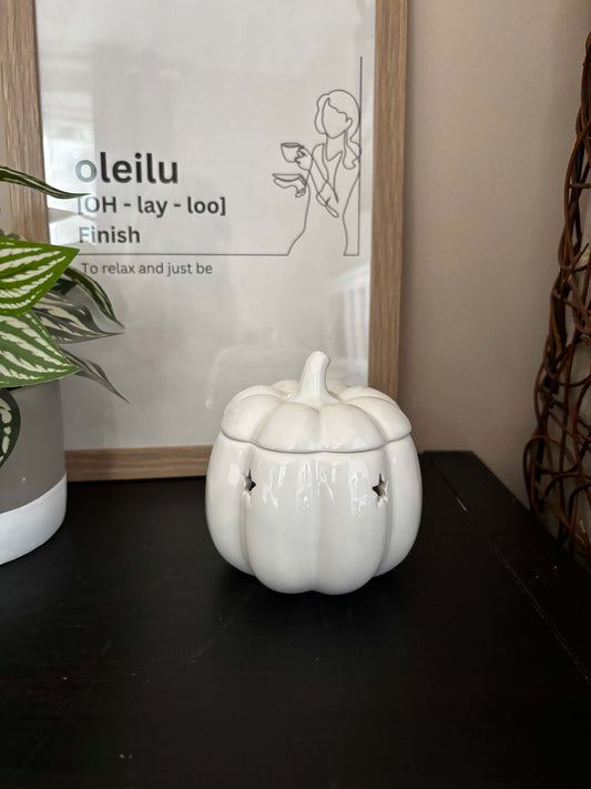 White ceramic pumpkin on a shelf with a decorative sign and plant in the background
