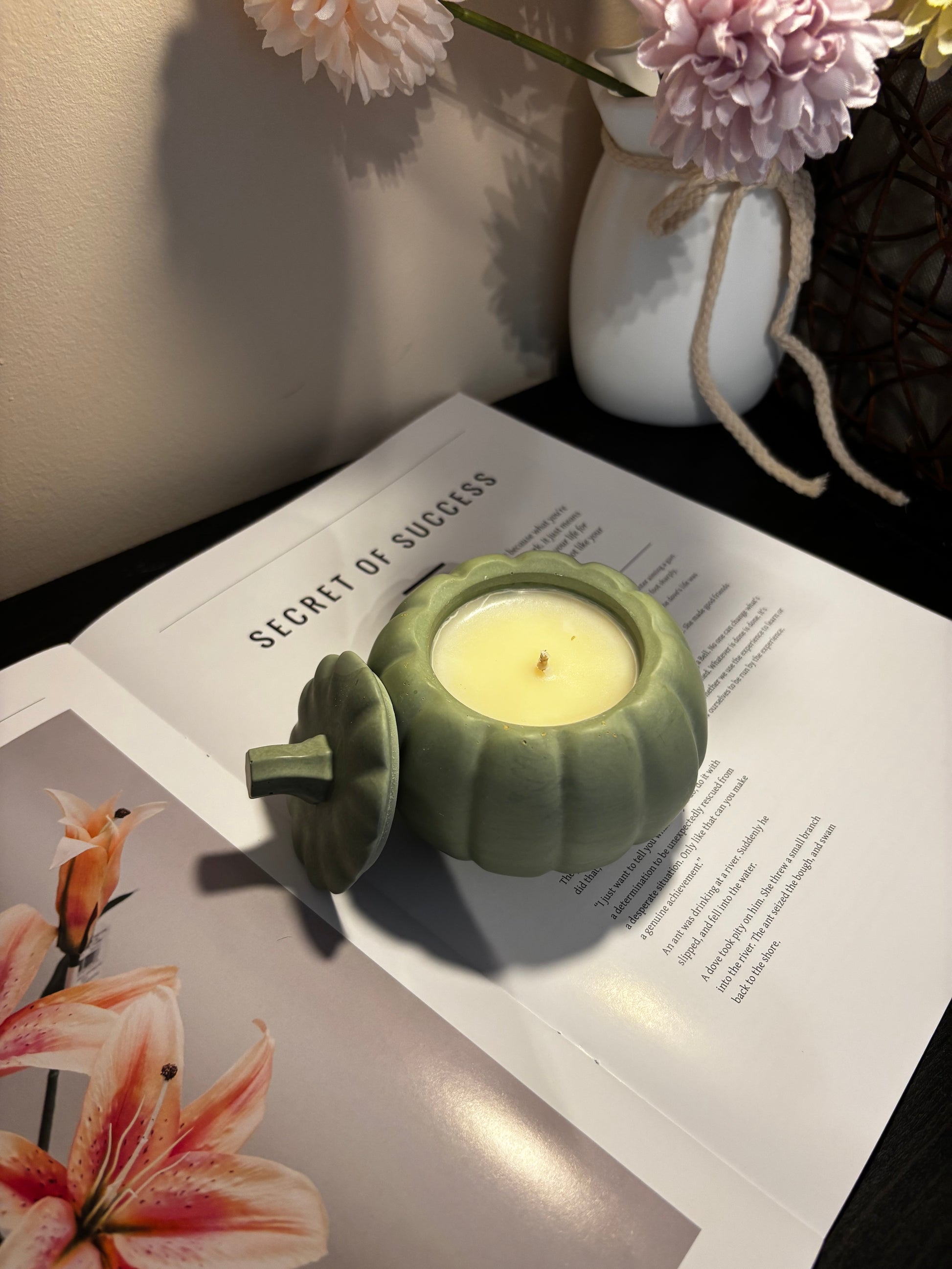 Green candle holder with a lit candle on an open book with floral illustrations