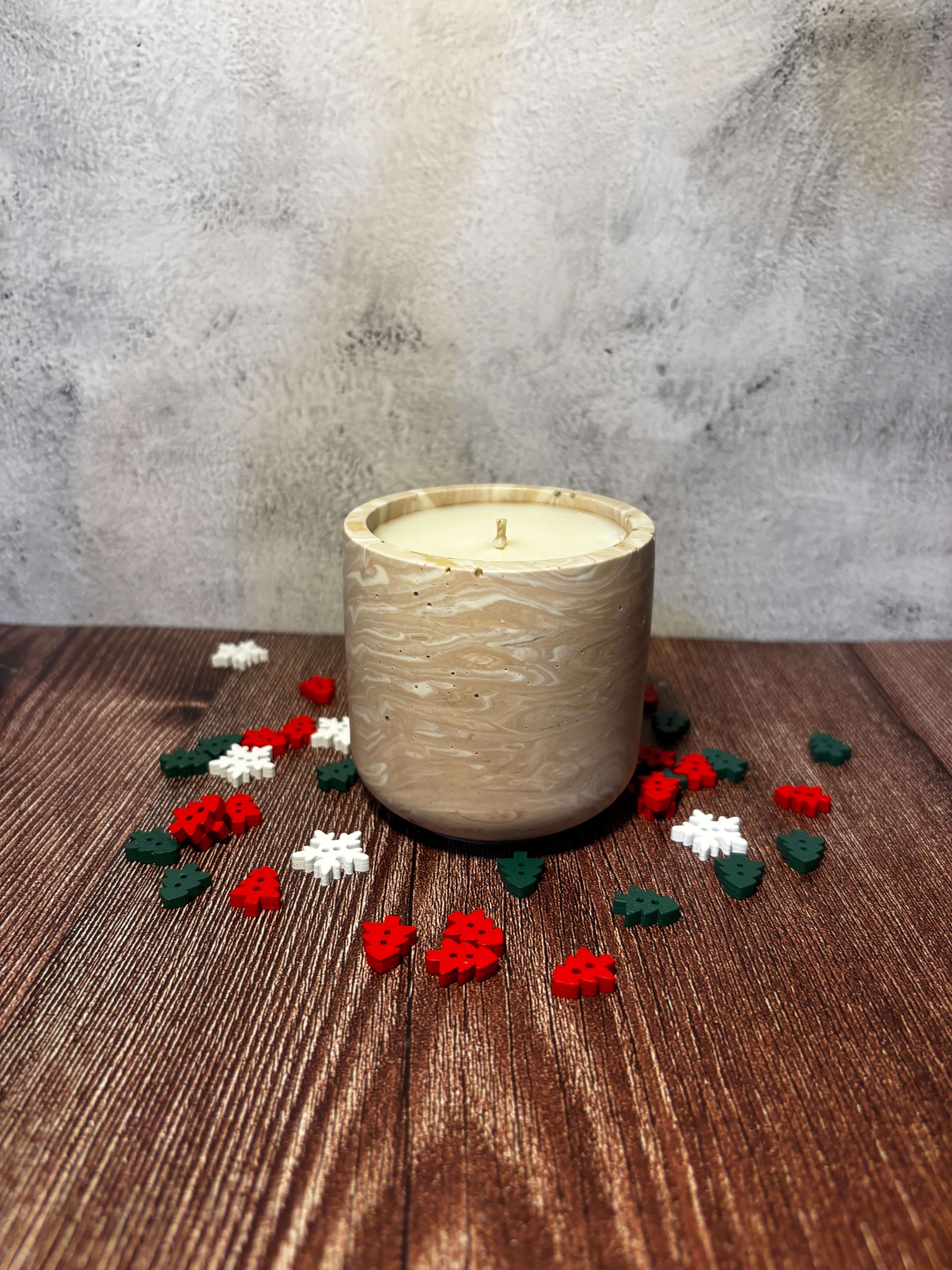 Alpine Lodges Candle in a beige holder with scattered red, white, and green flowers on a wooden surface.