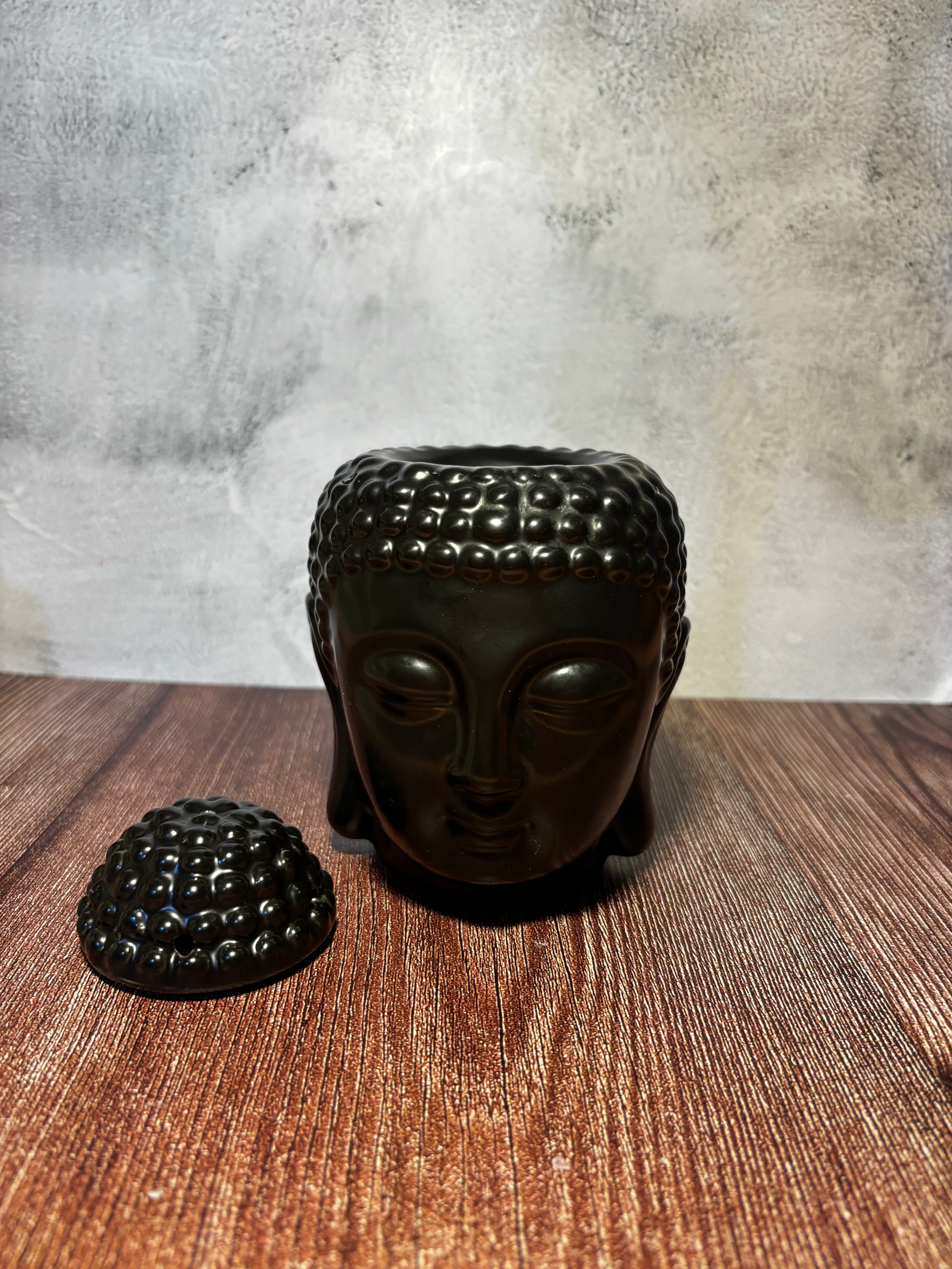 Black Buddha head incense burner on a wooden surface with a textured wall background
