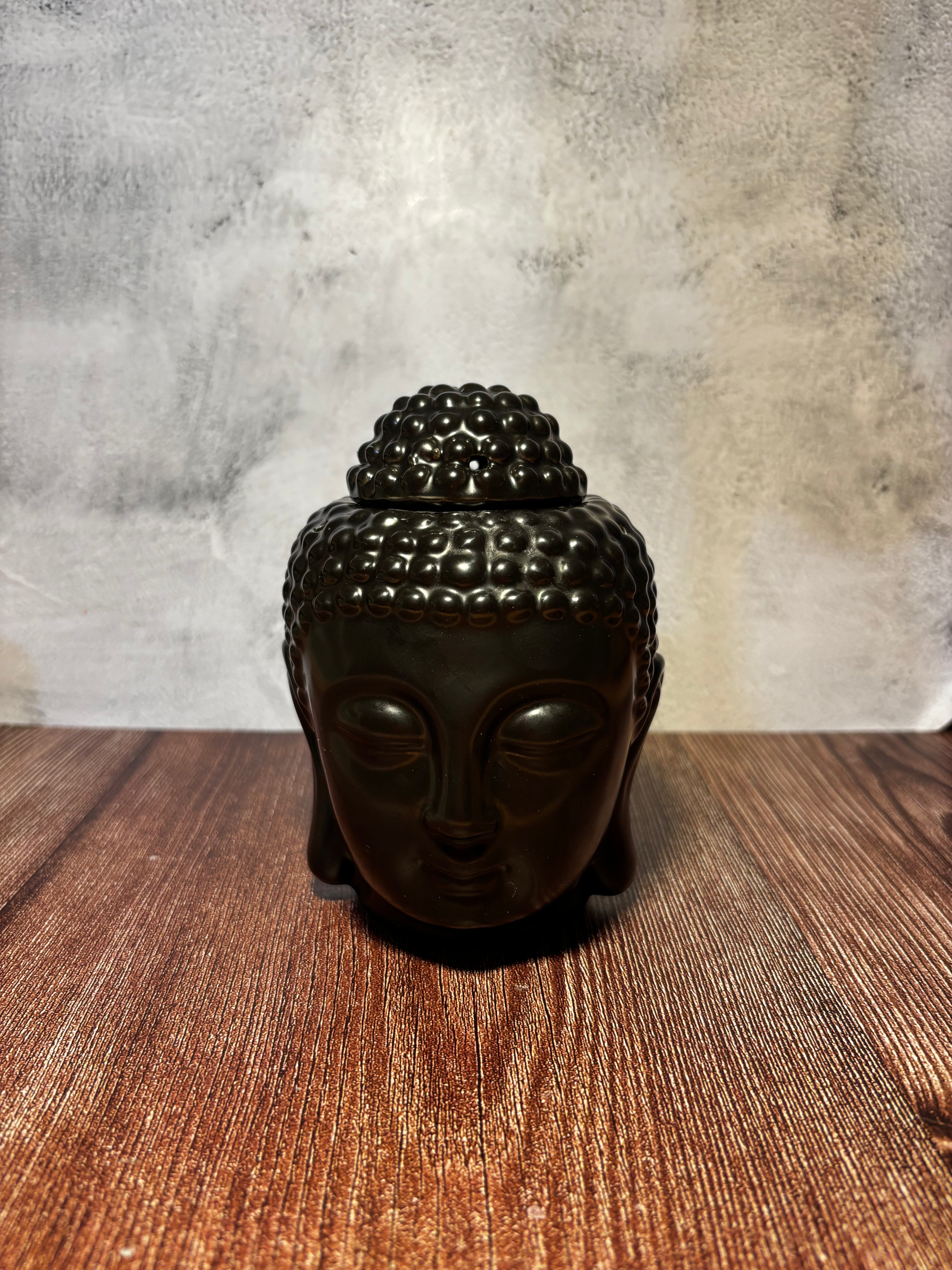 Black Buddha head sculpture on a wooden surface with a textured wall background