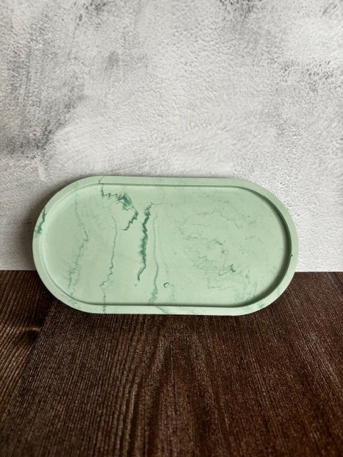 Green marble-patterned tray on a wooden surface with a concrete wall background