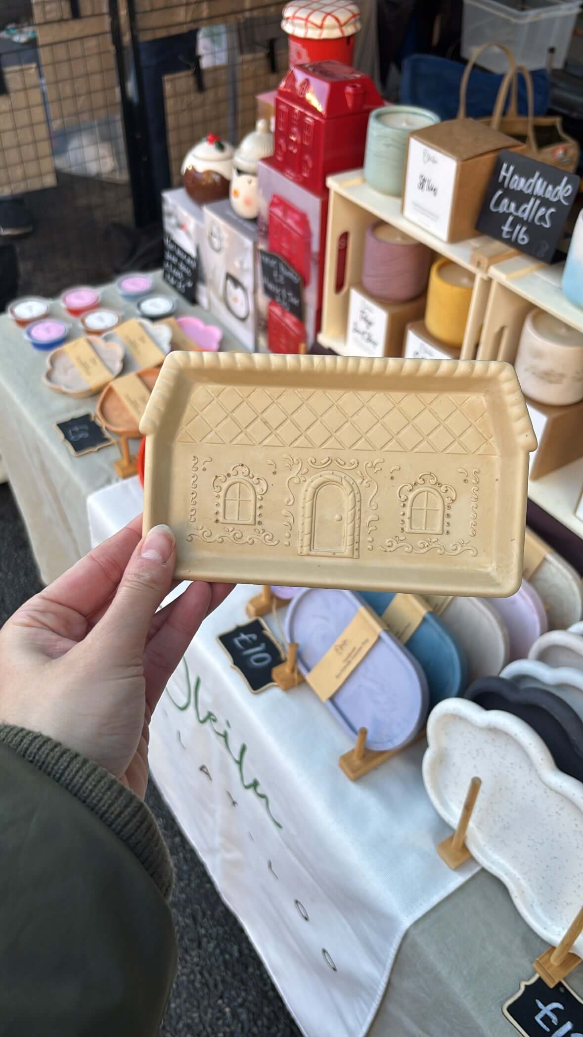 Hand holding a gingerbread tray with architectural design in a store setting.