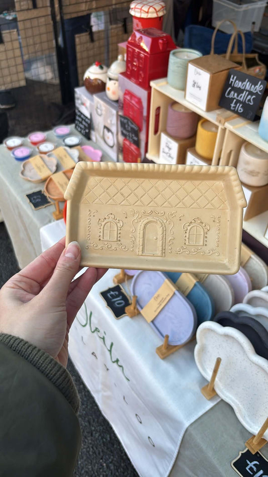 Hand holding a gingerbread tray with architectural design in a store setting.