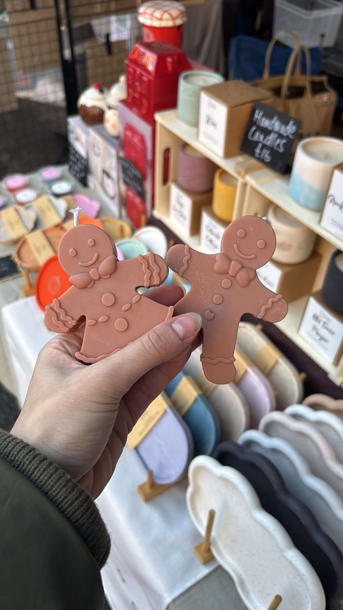 Hand holding two gingerbread men candles against a market stall background