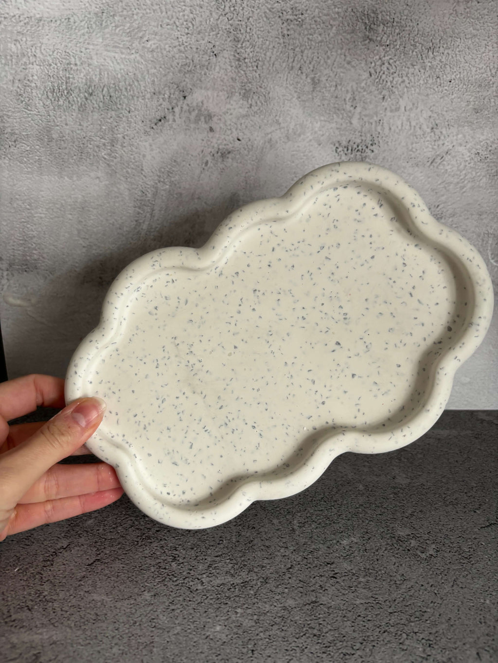 Hand holding a textured ceramic plate on a gray surface