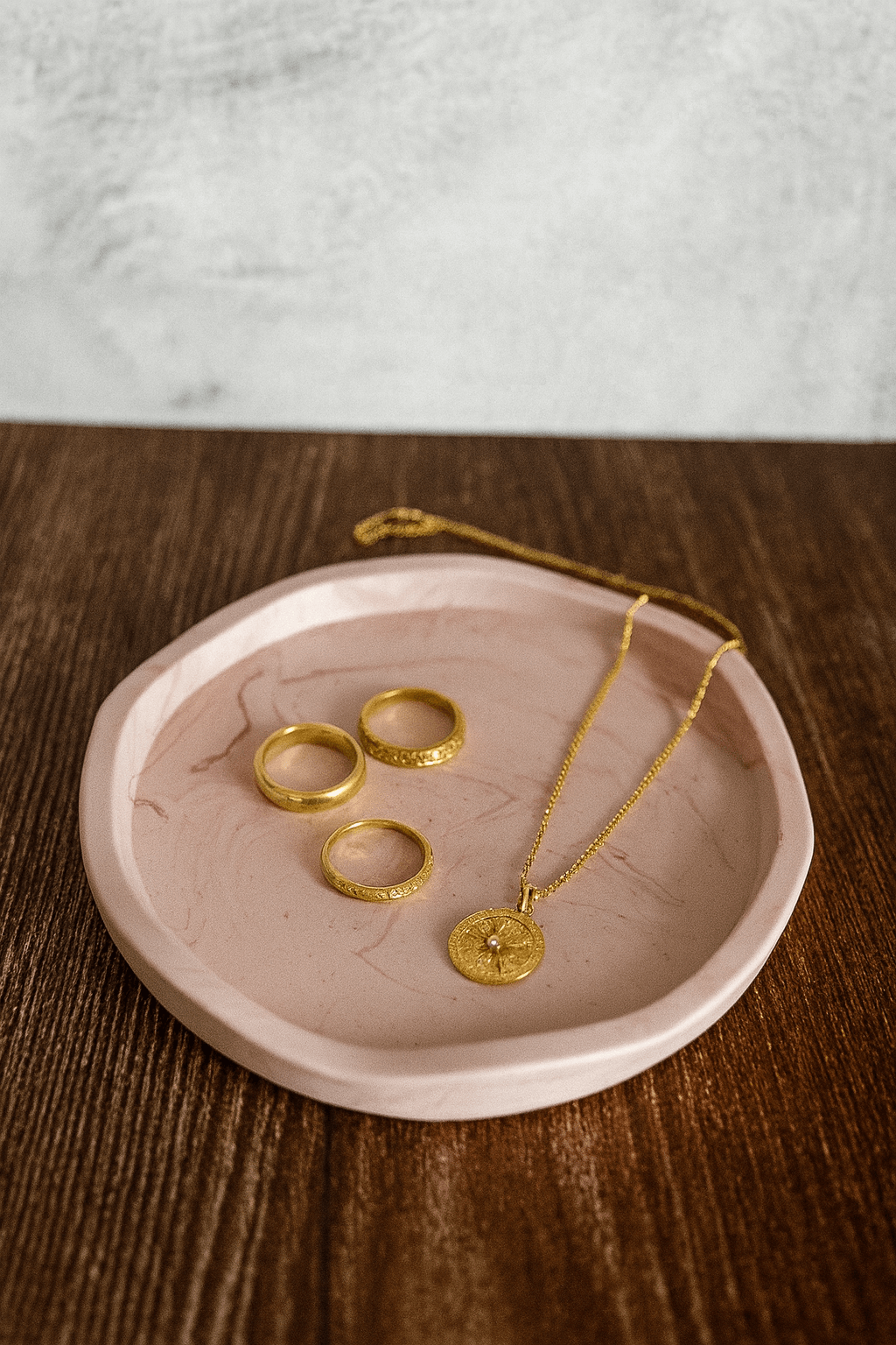 Pink jewelry dish with gold rings and necklace on a wooden surface