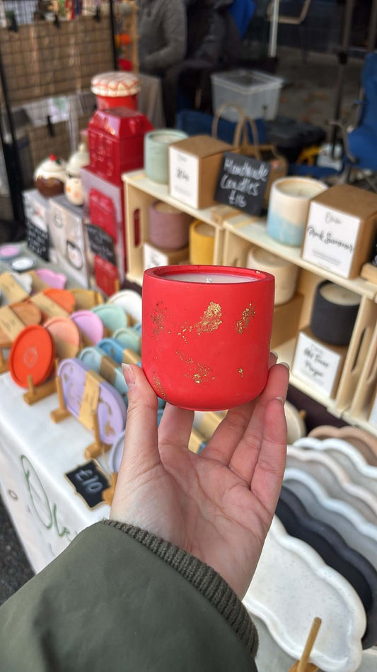 Red candle with gold designs held in front of a store display.