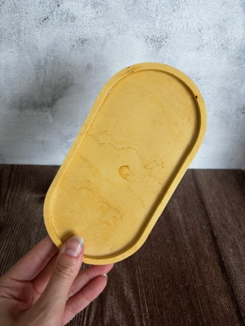 Yellow oval tray held by a hand against a textured gray and wooden background